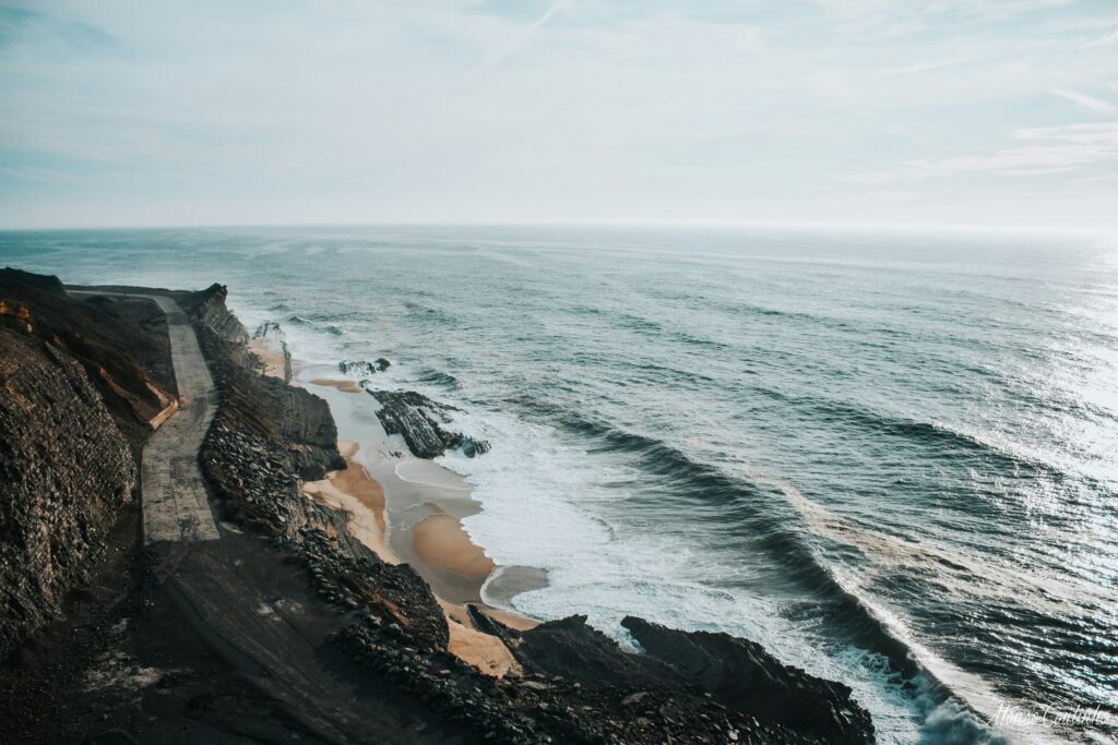 Pale surf washing over a dark rocky beach seen from above