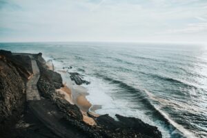 Pale surf washing over a dark rocky beach seen from above