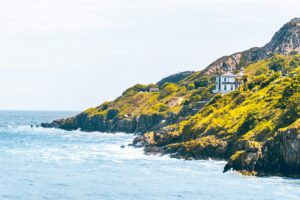Sunlit green cliffs and scattered houses above a bright blue sea