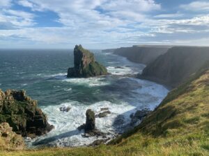 Sea stack and a long line of cliffs above a bay of breaking waves