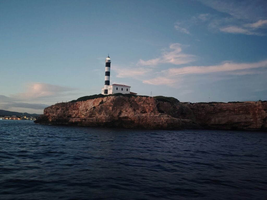 Black and white striped lighthouse on a low rocky island at dusk
