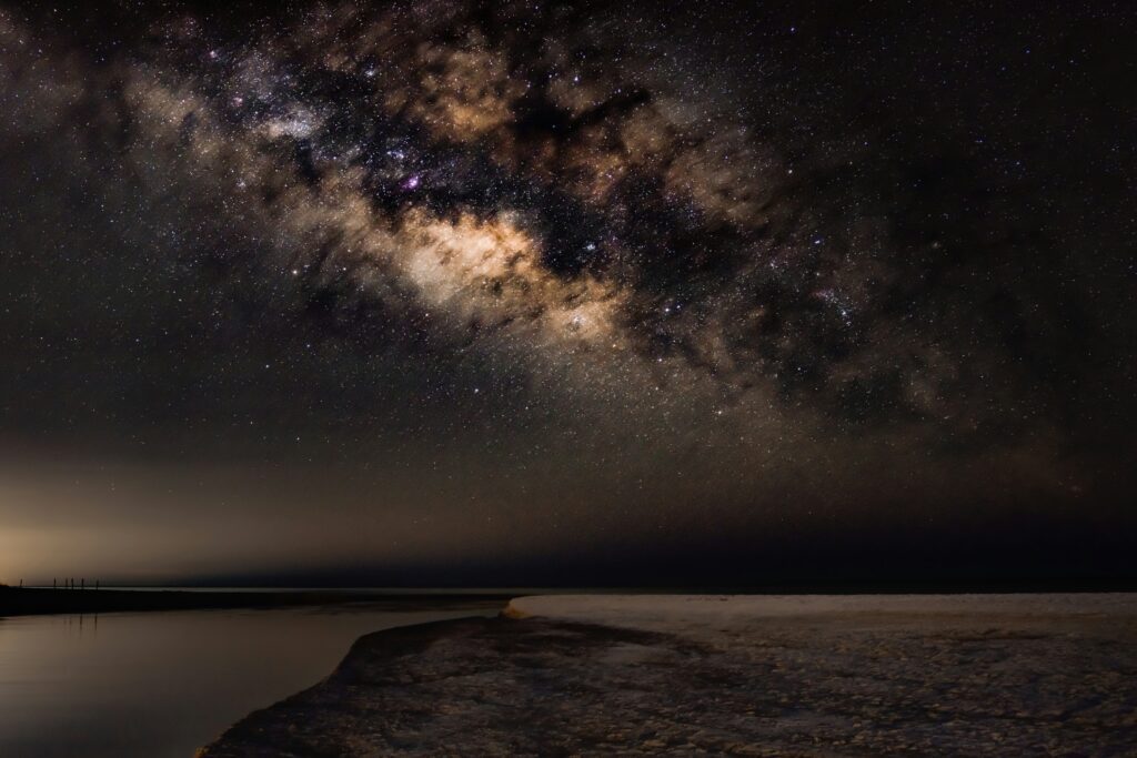 The Milky Way arching over a dark, empty beach