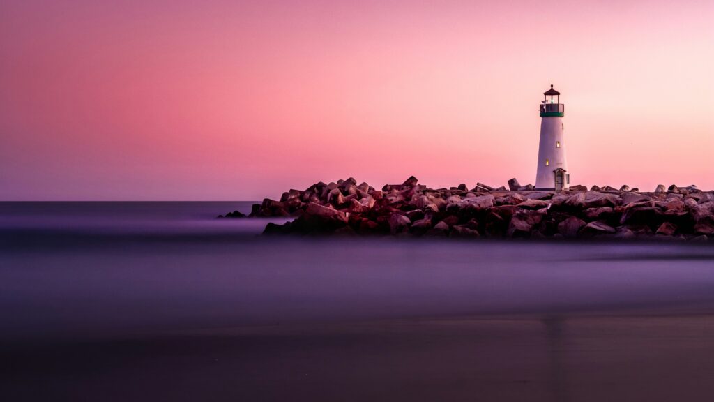Lighthouse on a rock breakwater beneath a pink and violet sunset