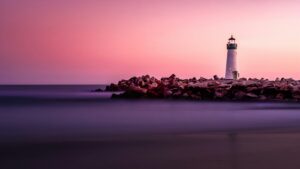 Lighthouse on a rock breakwater beneath a pink and violet sunset