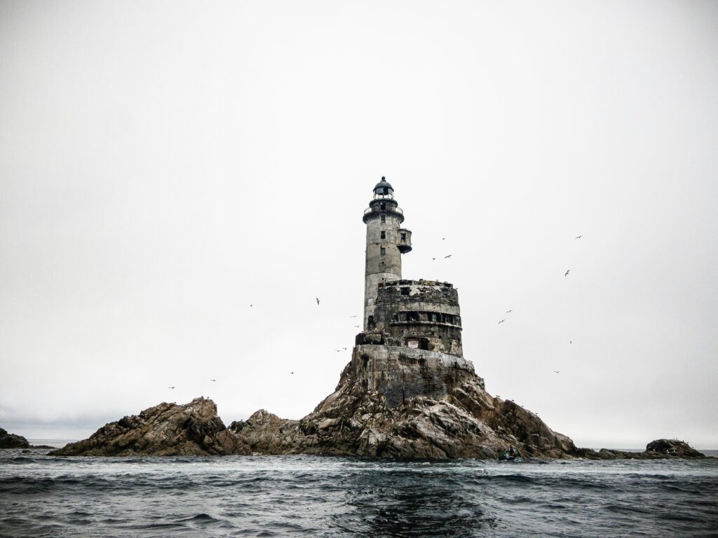 Ruined stone lighthouse on a sea-washed rock under a white sky