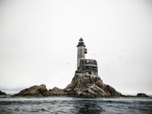 Ruined stone lighthouse on a sea-washed rock under a white sky