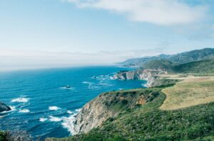 Turquoise water below green coastal hills under a hazy sky