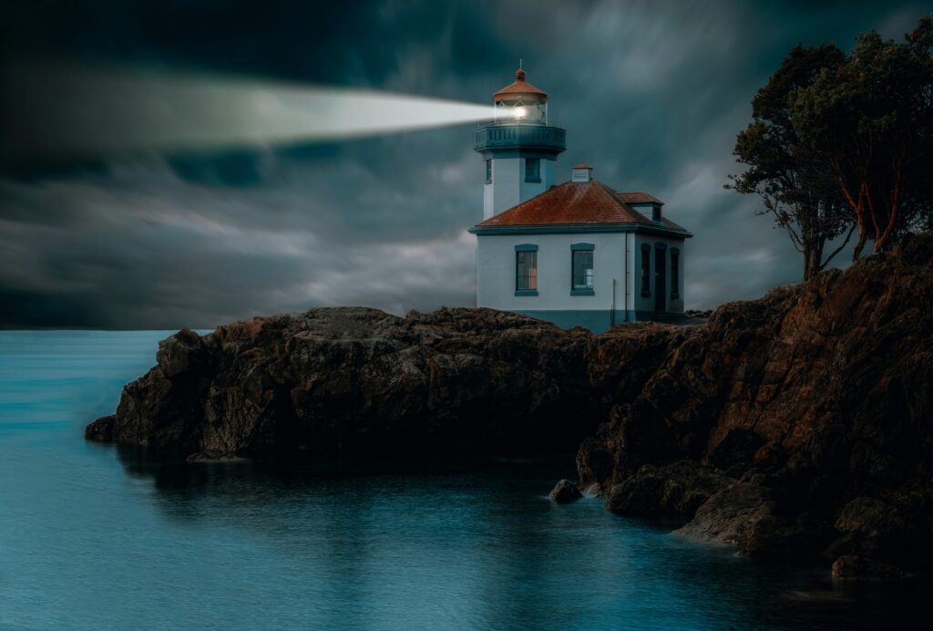 Lighthouse beam cutting through night fog above dark rocks