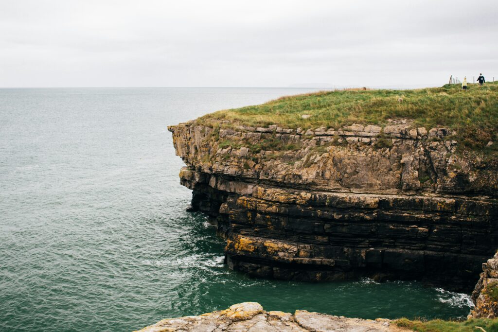 Layered limestone cliff jutting out over green water