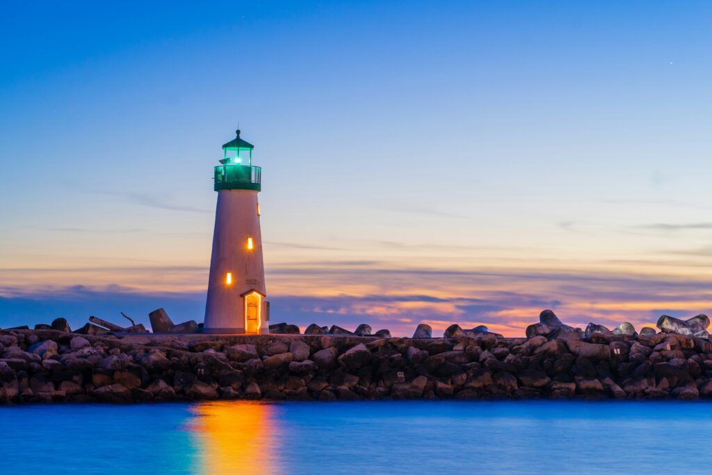 Lighthouse with a green lantern glowing above a rock breakwater at sunset