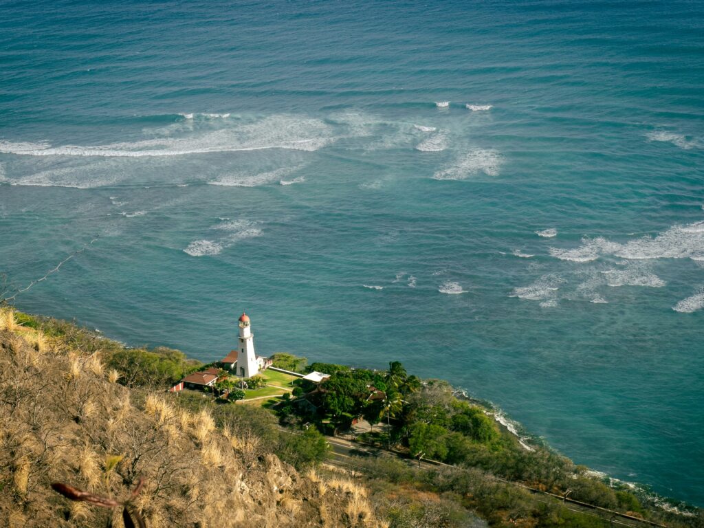 Small white lighthouse on a green headland above turquoise surf