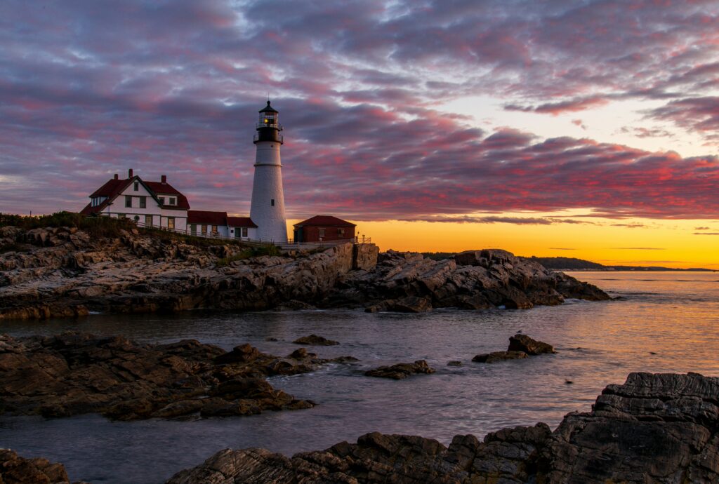 Portland Head Light above a rocky shoreline beneath a violet sunrise
