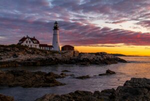 Portland Head Light above a rocky shoreline beneath a violet sunrise