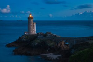 Stone lighthouse lit at dusk on a rocky point joined by a causeway