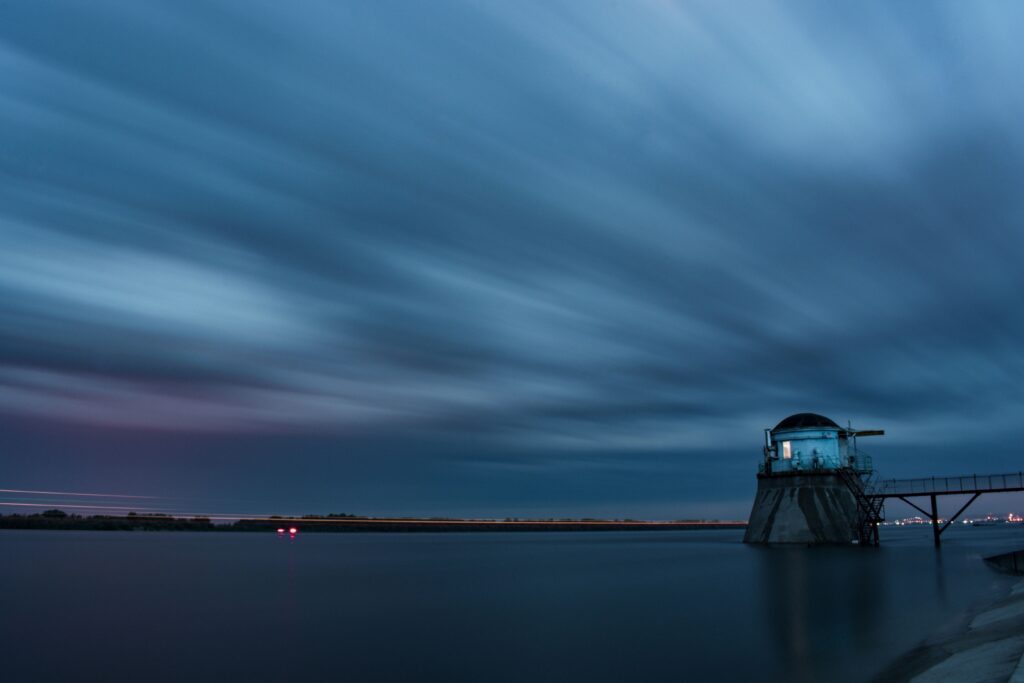 Long exposure of a lighthouse at the end of a causeway under streaked cloud