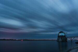 Long exposure of a lighthouse at the end of a causeway under streaked cloud