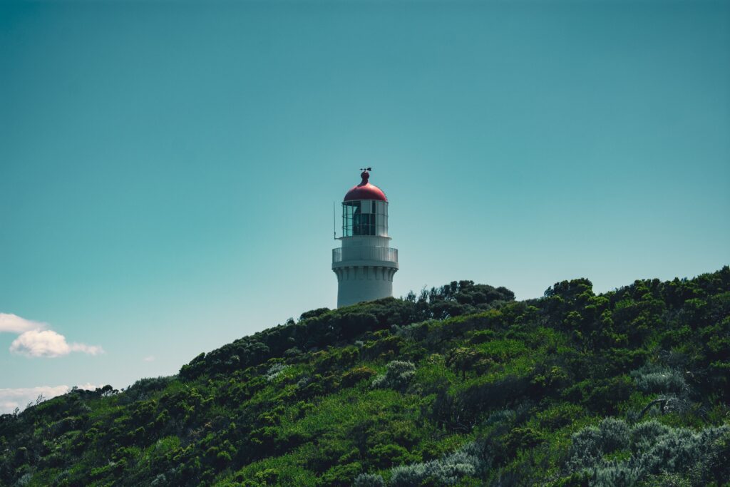 White lighthouse with a red lantern room on a grassy headland