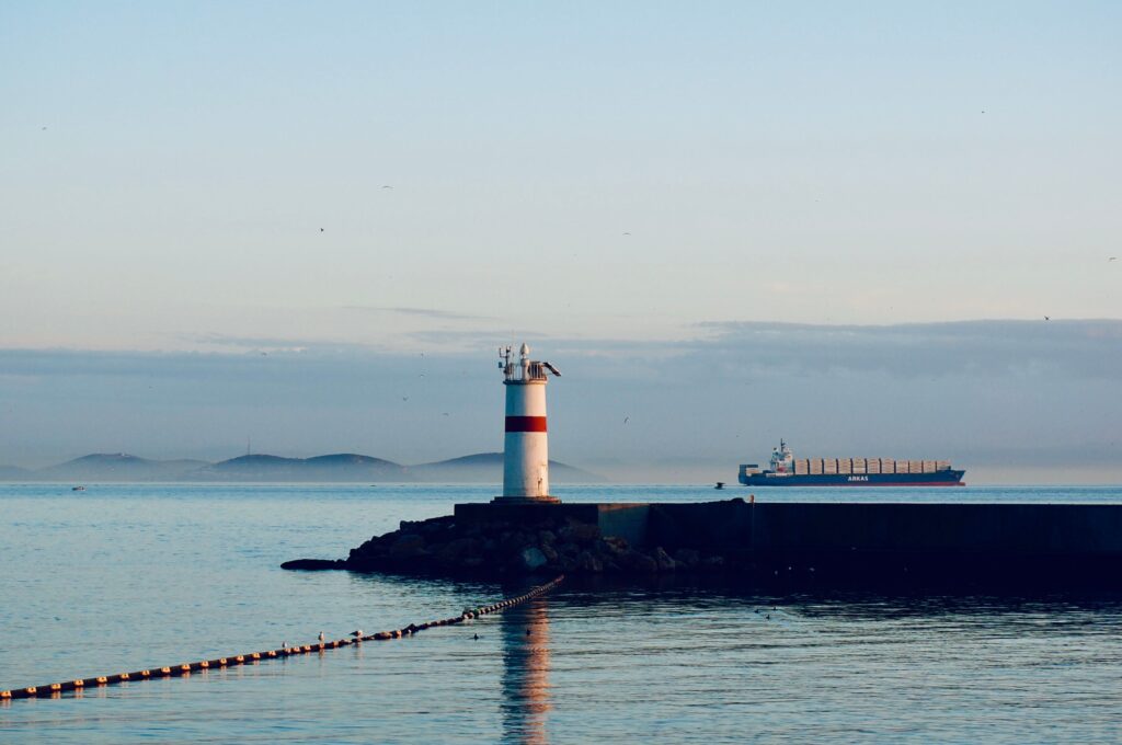 Red and white harbour light on a breakwater as a cargo ship passes