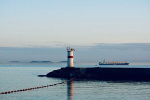 Red and white harbour light on a breakwater as a cargo ship passes