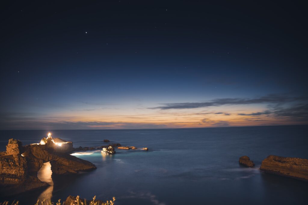 Lit lighthouse on a rocky point under a deep blue dusk sky