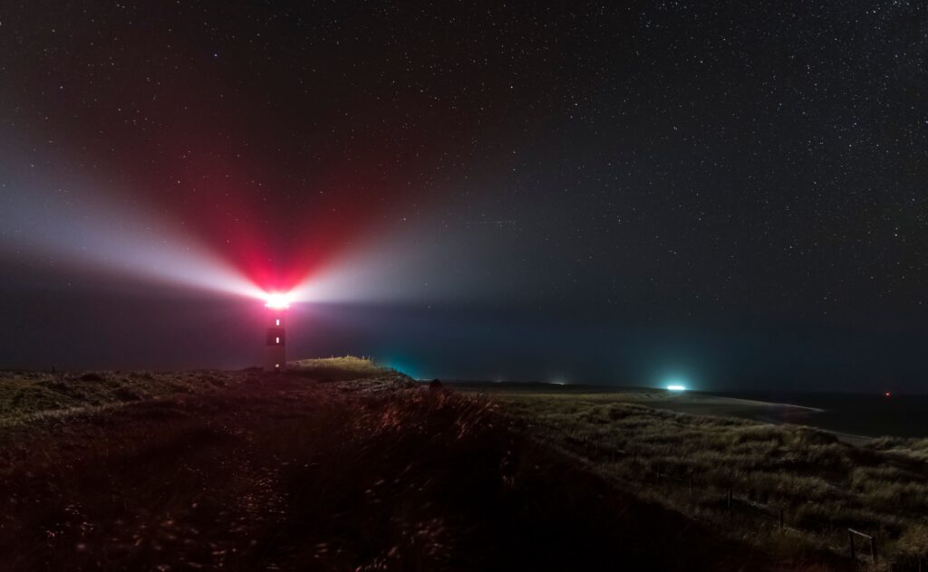 Red lighthouse beam sweeping across a dark headland at night