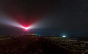 Red lighthouse beam sweeping across a dark headland at night