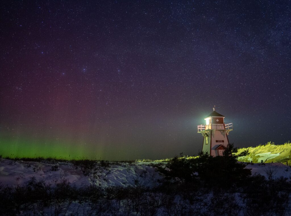 White lighthouse under a starry sky with green aurora on the horizon