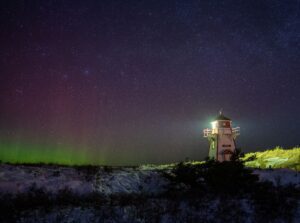 White lighthouse under a starry sky with green aurora on the horizon