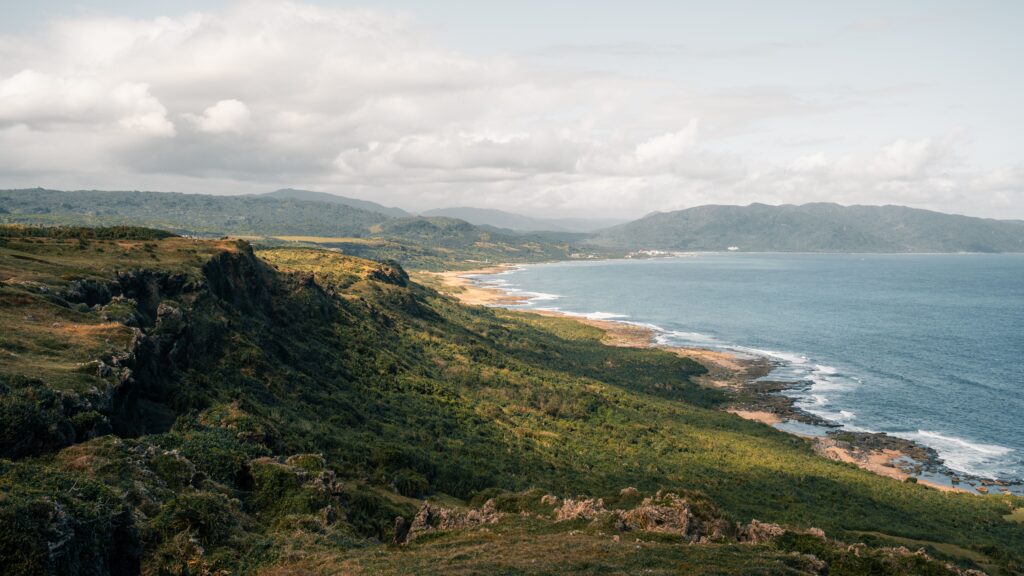 Green coastal hills above a curving beach with a village in the distance
