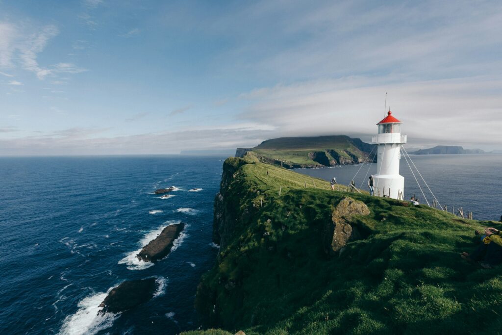White lighthouse on a green clifftop above a deep blue sea