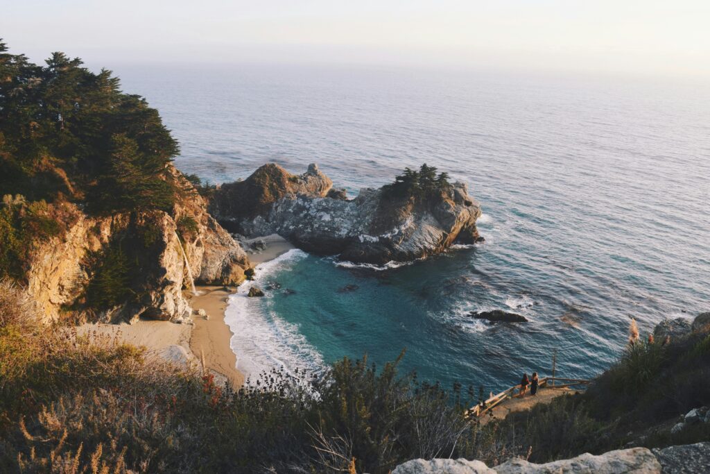 Cove with a waterfall spilling onto a sandy beach below forested cliffs