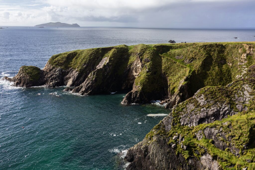 Green clifftop and rock arch above deep blue water