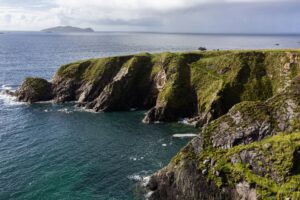 Green clifftop and rock arch above deep blue water