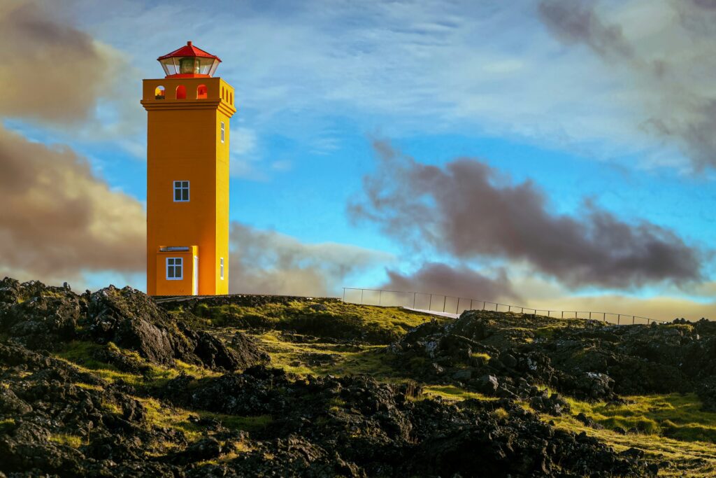Yellow lighthouse tower on a green clifftop with dark cloud behind