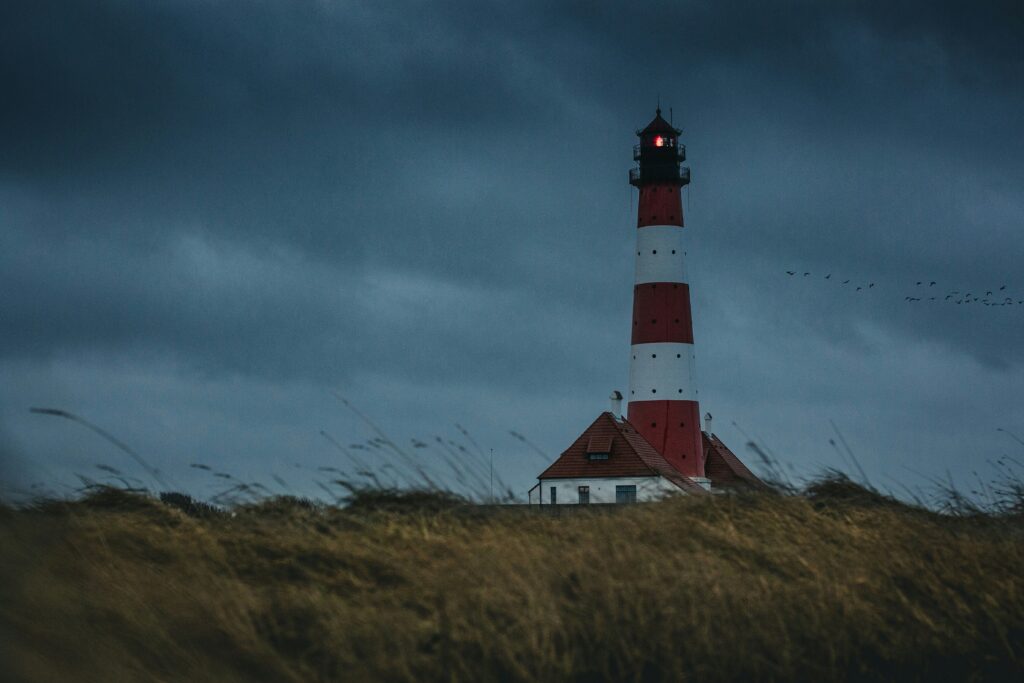 Red and white lighthouse on a windswept dune under a stormy sky