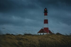 Red and white lighthouse on a windswept dune under a stormy sky